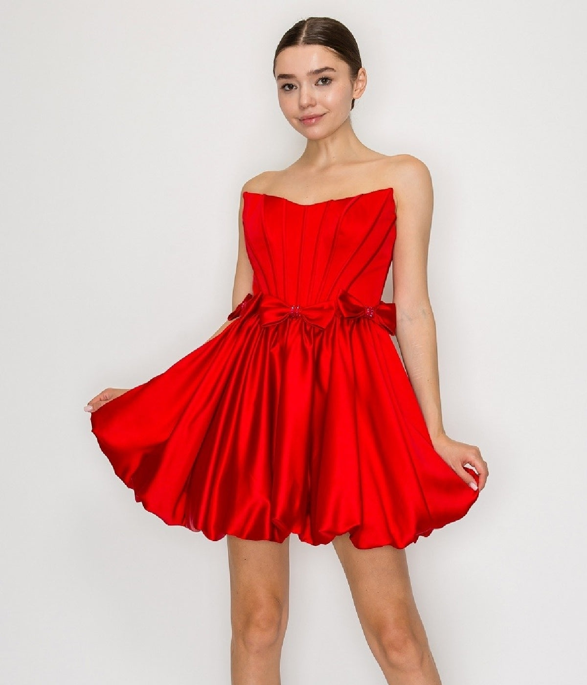 A woman models the Poly USA 9950 Strapless Short Bubble Party Dress in red, featuring a corset-style bodice and flared skirt, standing against a plain white background.